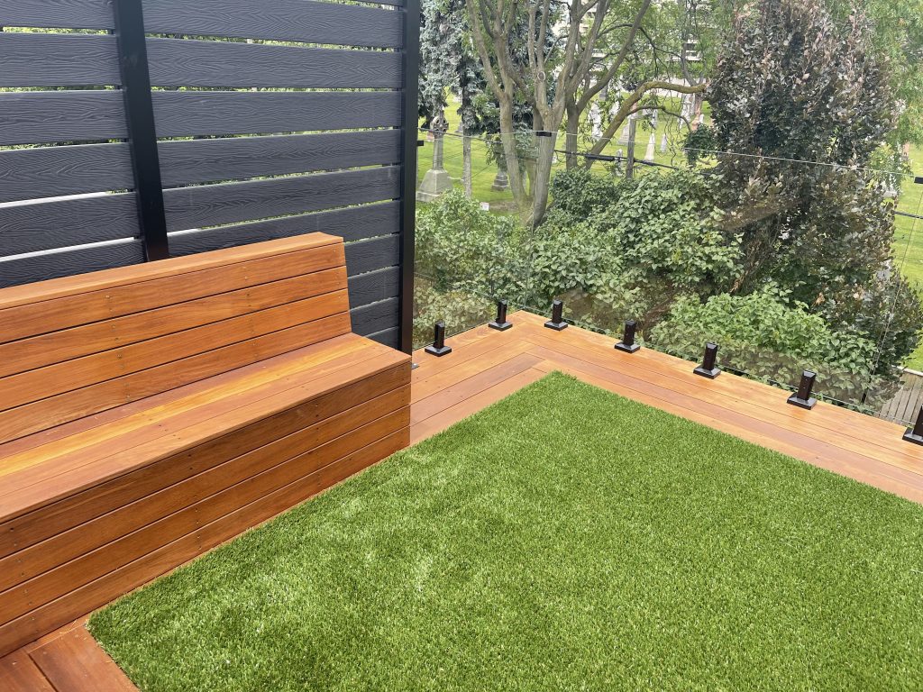 Modern outdoor seating area with wooden bench, artificial grass, and glass railing, showcasing quality exterior renovation by Urban Reno Design.